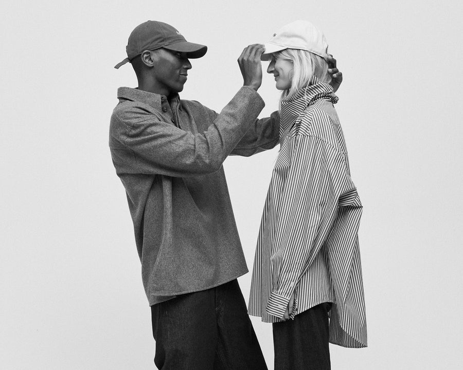 Black and white photo of two friends trying on Artless organic cotton caps together, from the Artless: the People campaign