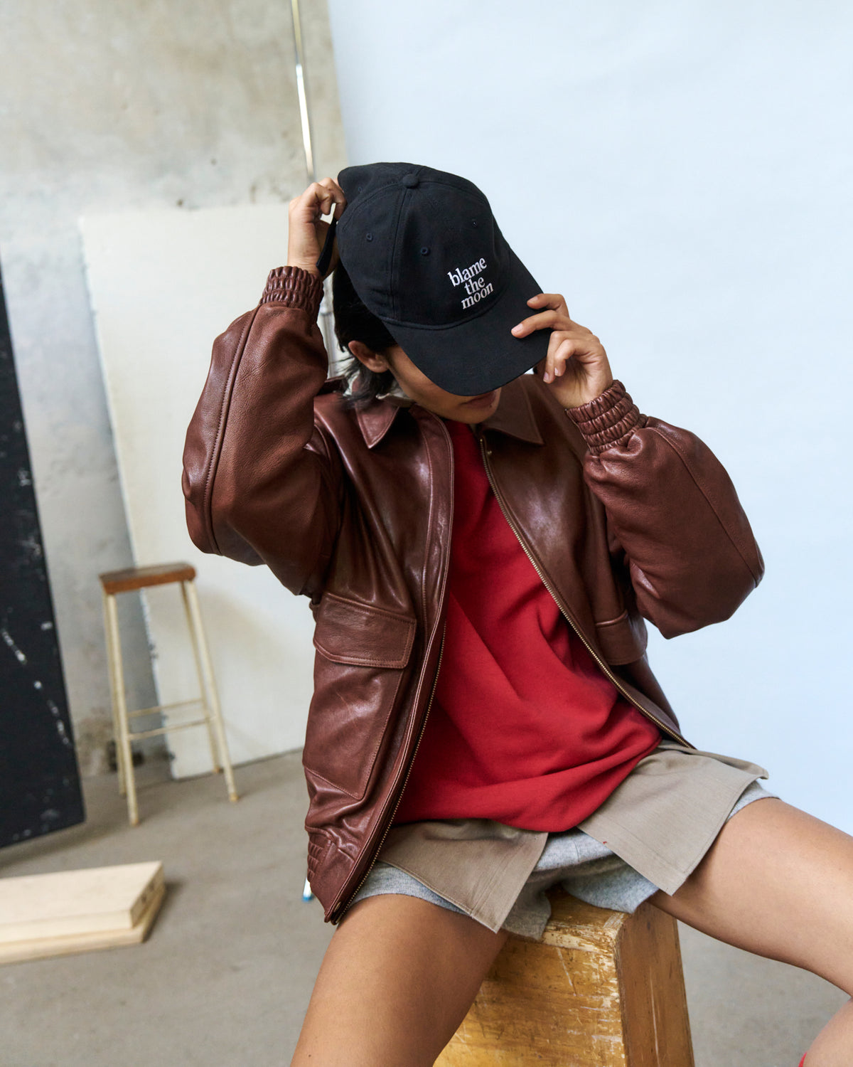 Person in a brown leather jacket pulling the black Artless Blame the Moon organic cotton dad cap down over their face