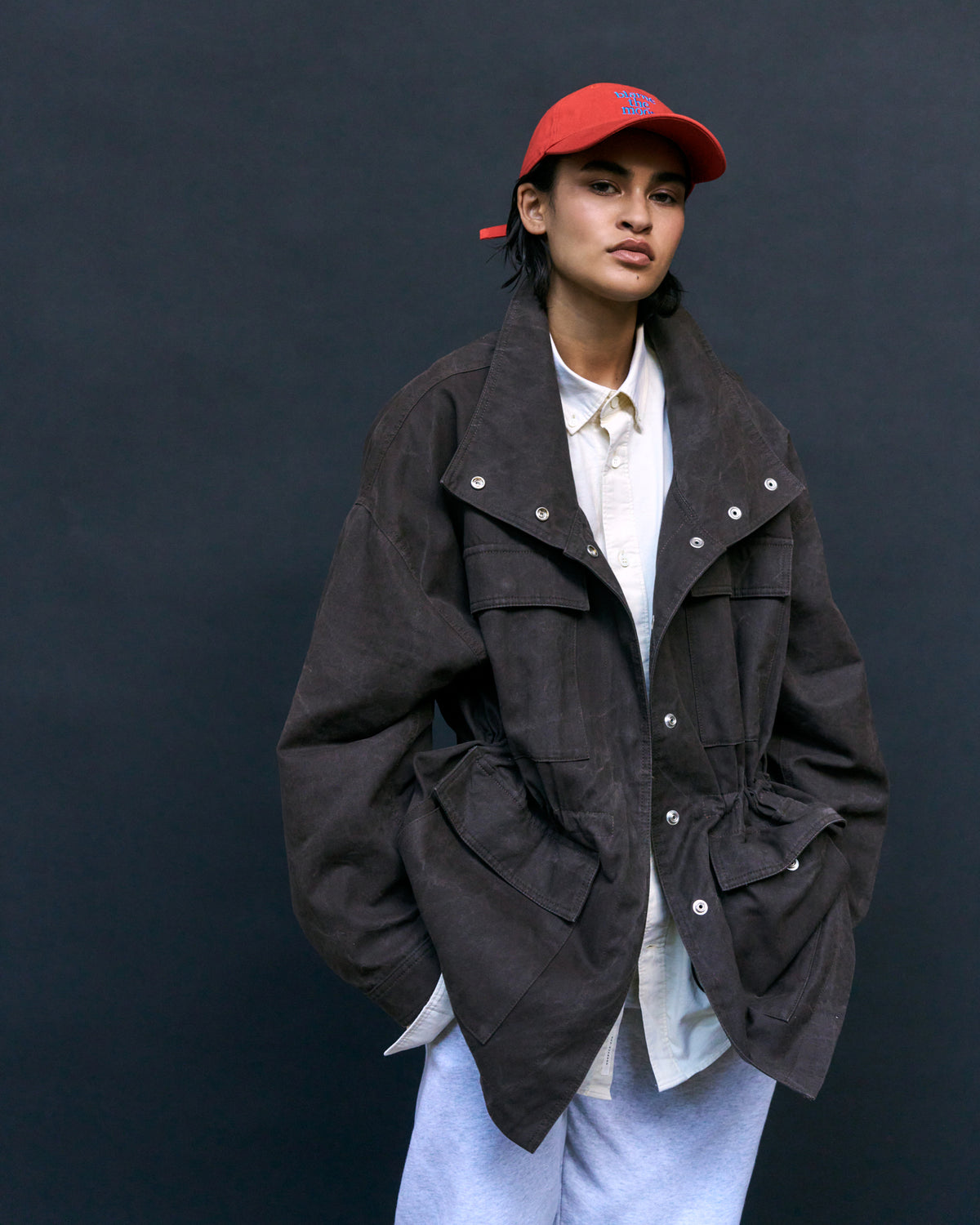 Person wearing the red Artless Blame the Moon organic cotton dad cap and an oversized brown jacket, full length studio shot