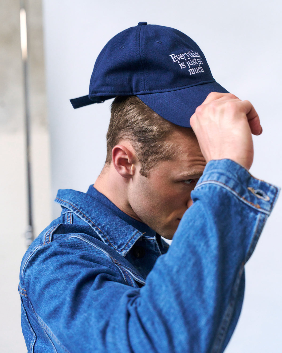 Man in a denim shirt adjusting the navy Artless Everything Is Just So Much organic cotton dad cap on his head