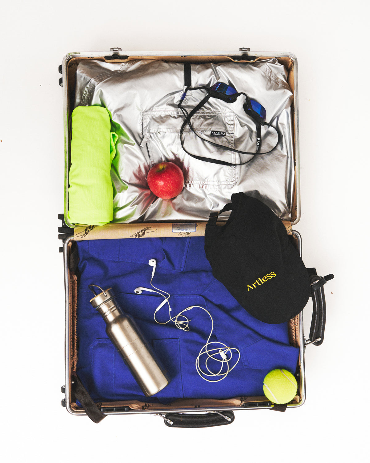Open suitcase packed with travel essentials styled with Artless organic cotton pieces, flat lay on a light background