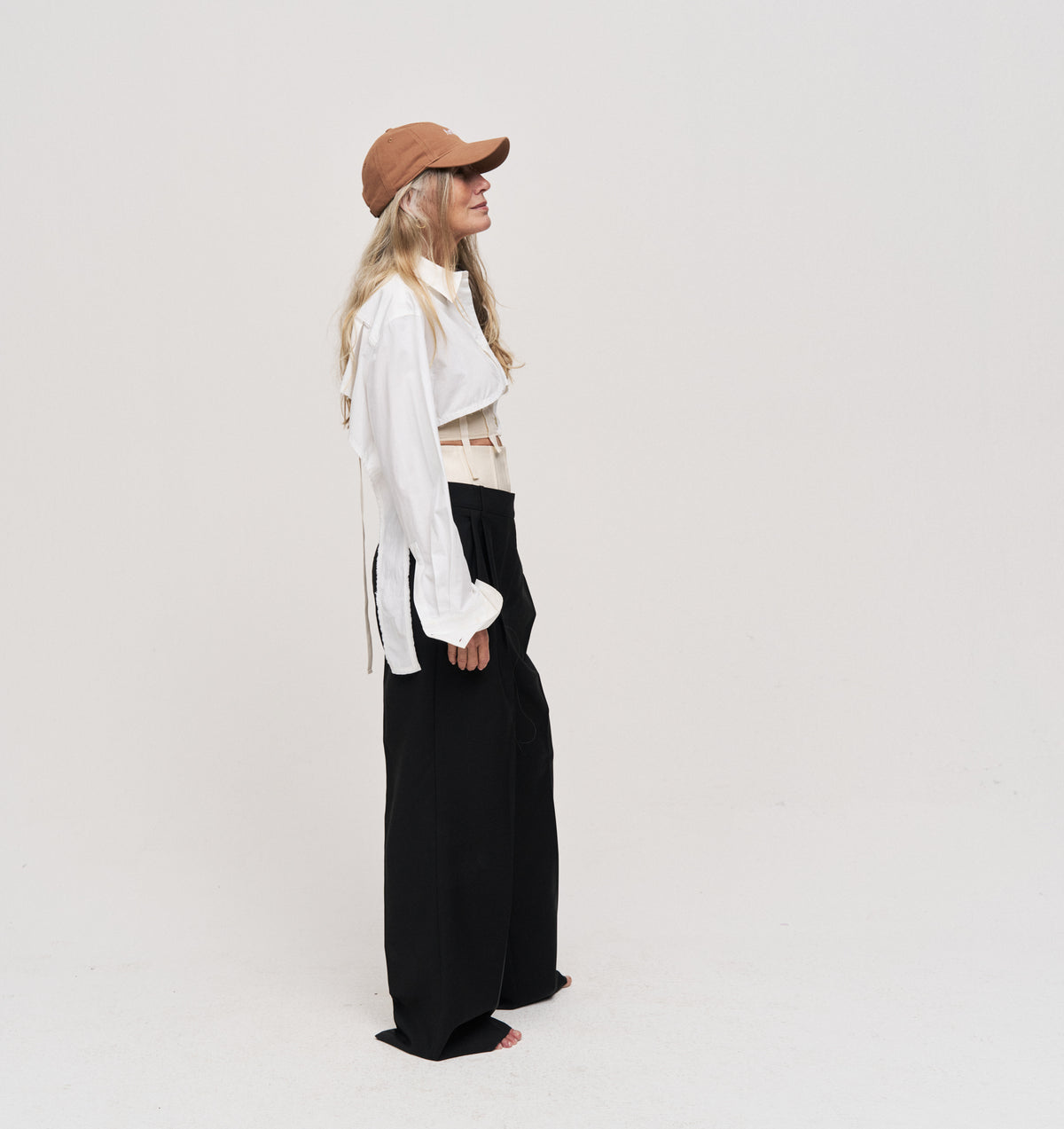 Person standing in profile wearing the brown Artless organic cotton logo dad cap, white shirt and black trousers