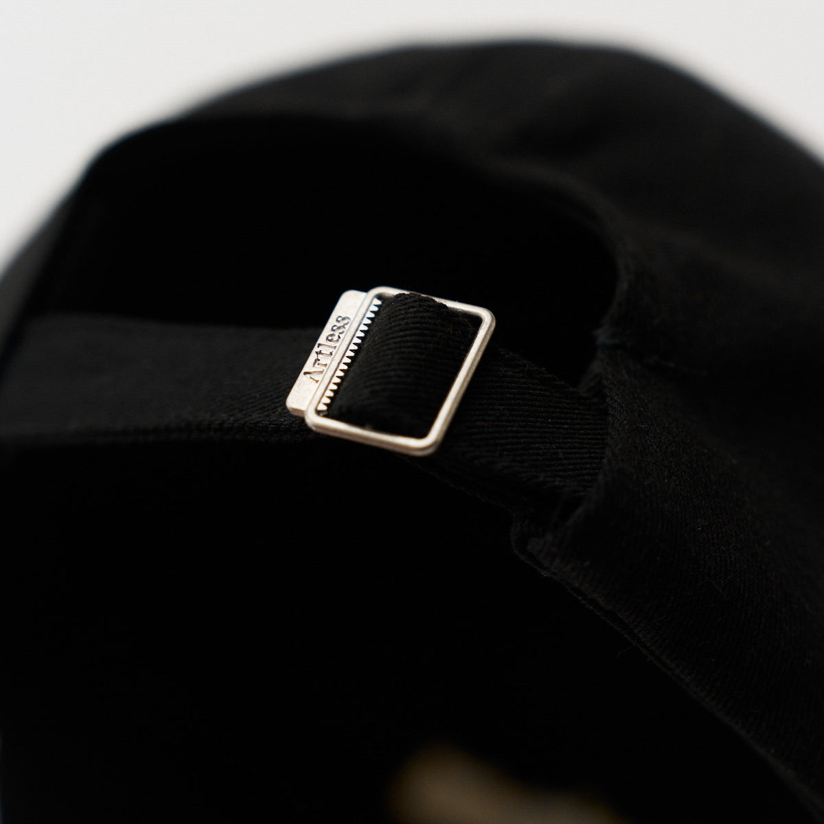 Close-up of the engraved Artless buckle on the black unstructured 6-panel dad cap made from GOTS certified organic cotton