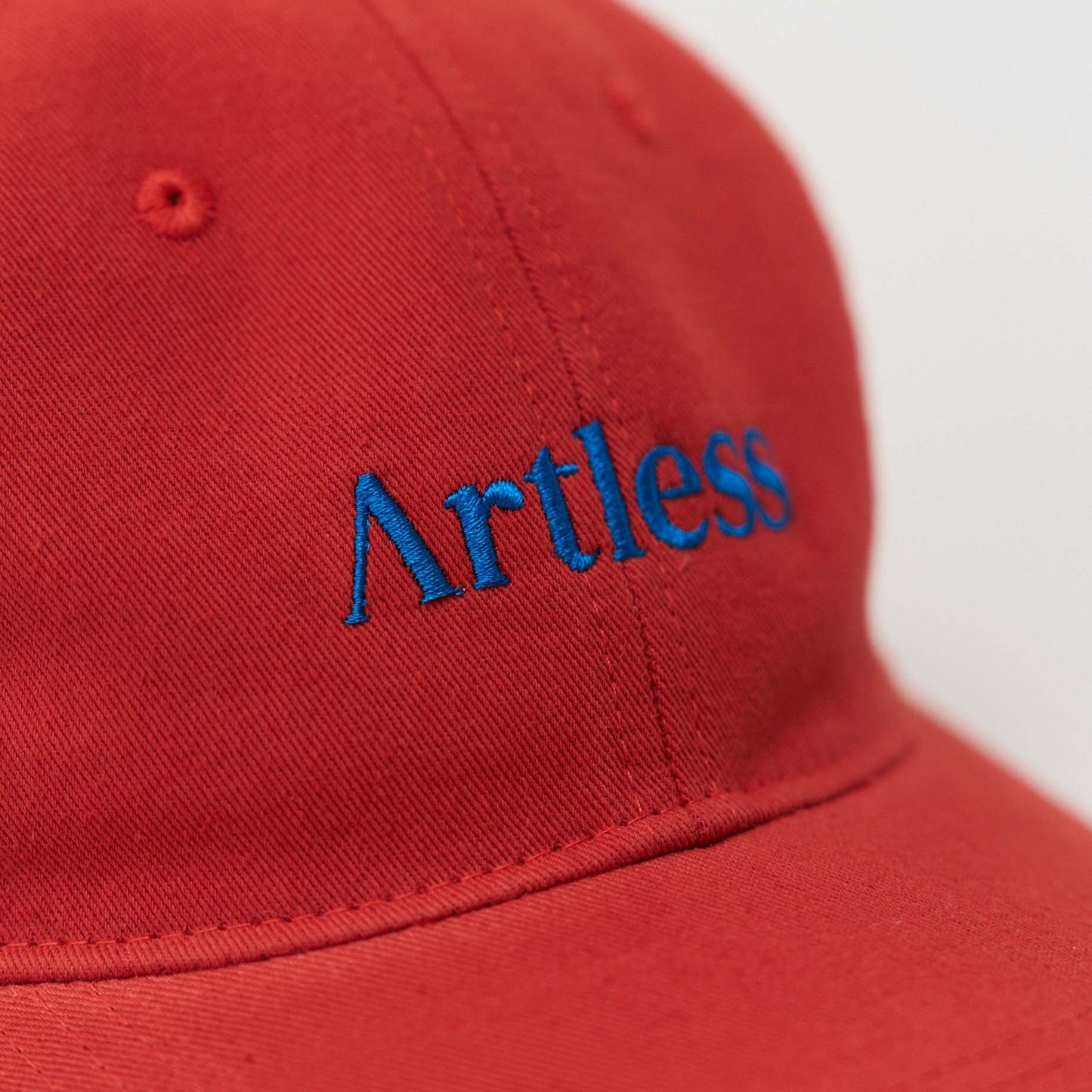 Close up of a Red unstructured 6-panel dad cap made from GOTS certified organic cotton by Artless with a blue logo