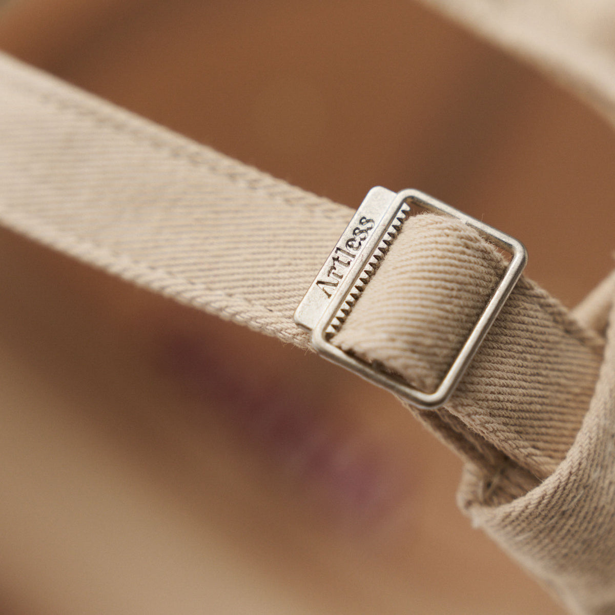 Close-up of the engraved Artless buckle on the sand coloured unstructured 6-panel dad cap made from GOTS certified organic cotton