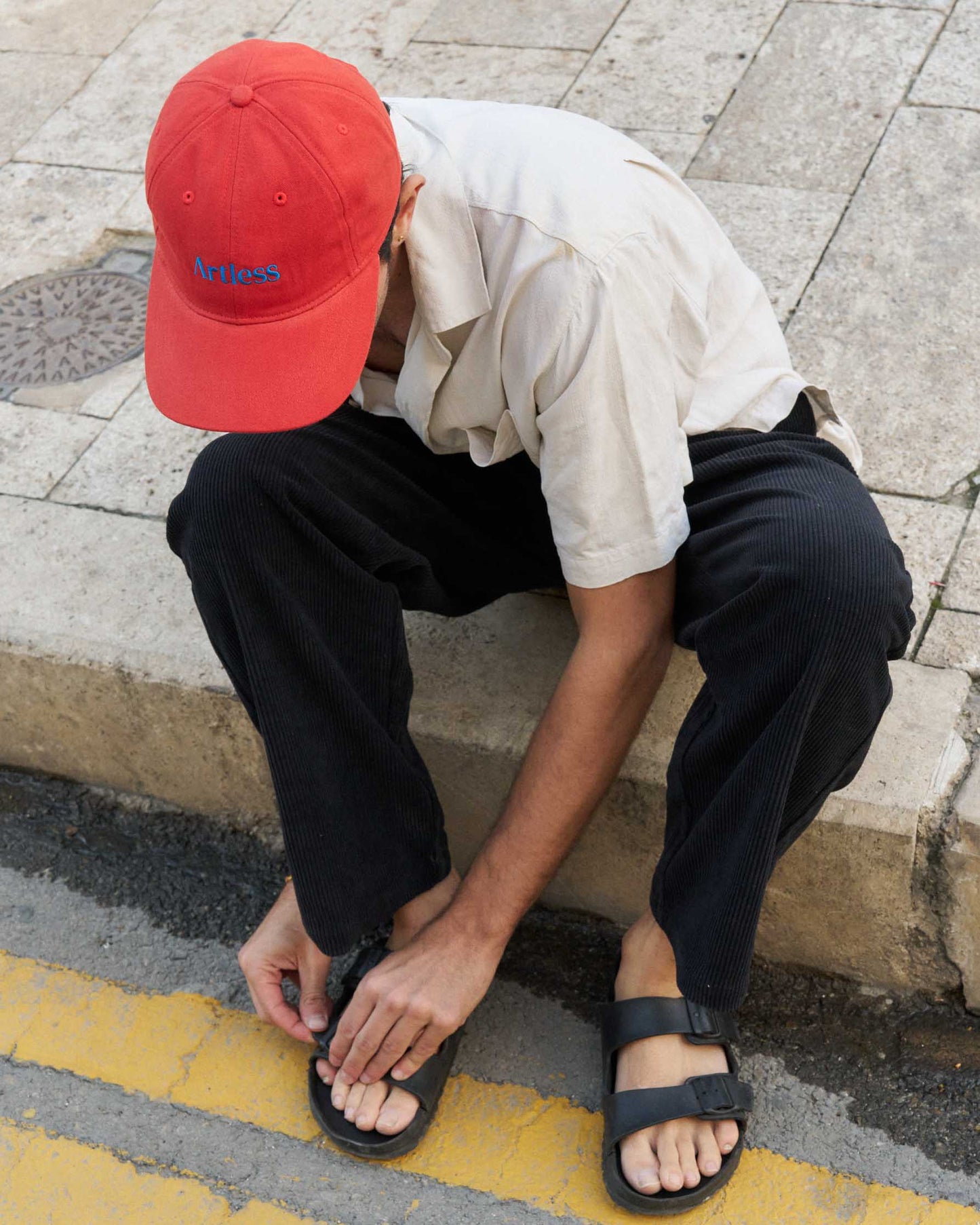 Person wearing a red unstructured 6-panel dad cap made from GOTS certified organic cotton by Artless sitting on a sidewalk