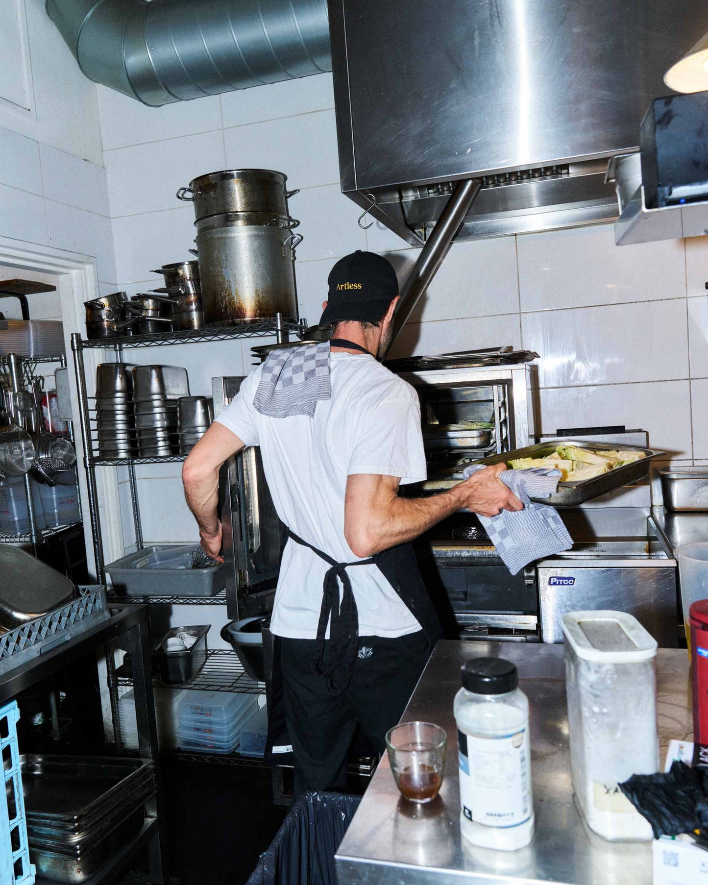 Person working in a restaurant kitchen with stainless steel equipment wearing black unstructured 6-panel dad cap made from GOTS certified organic cotton by Artless