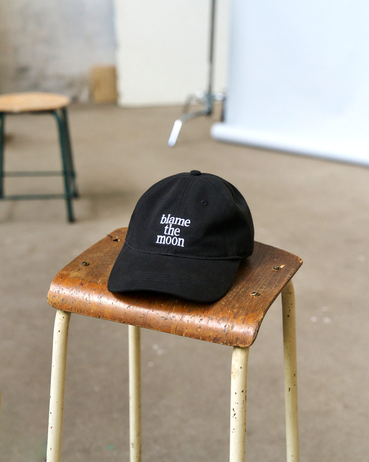 Black Artless Blame the Moon organic cotton dad cap with white embroidery resting on a wooden stool in a studio