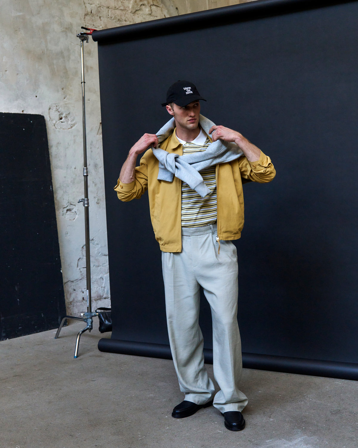 Man pulling on a yellow jacket while wearing the black Artless Blame the Moon organic cotton dad cap, studio backdrop