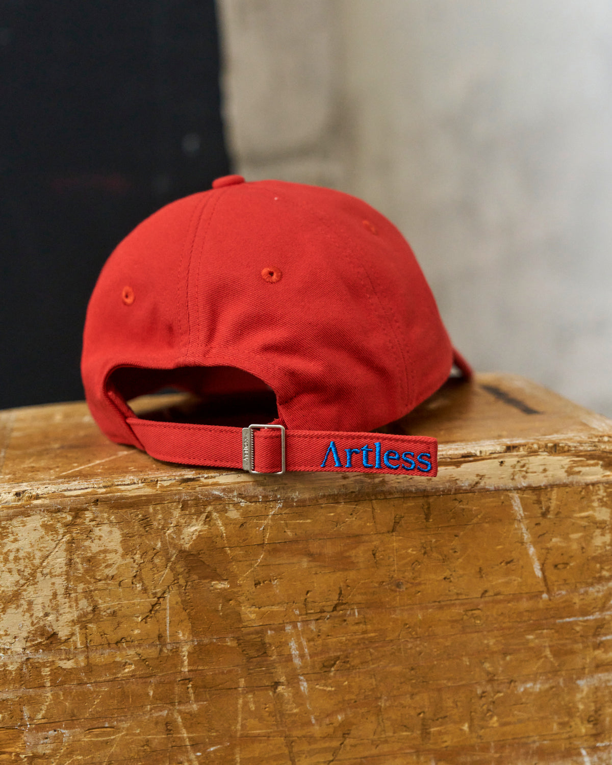 Red Artless Blame the Moon organic cotton dad cap resting on a wooden block, back view showing the embroidered Artless strap