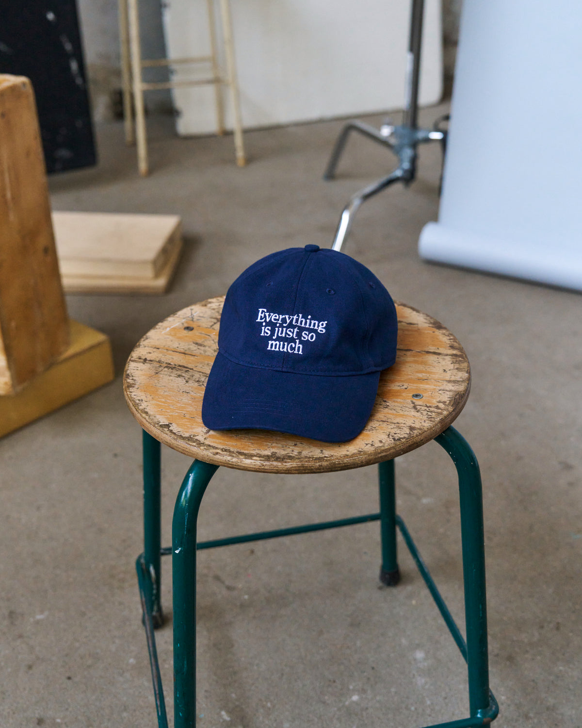 Navy Artless Everything Is Just So Much organic cotton dad cap resting on a wooden stool in a studio