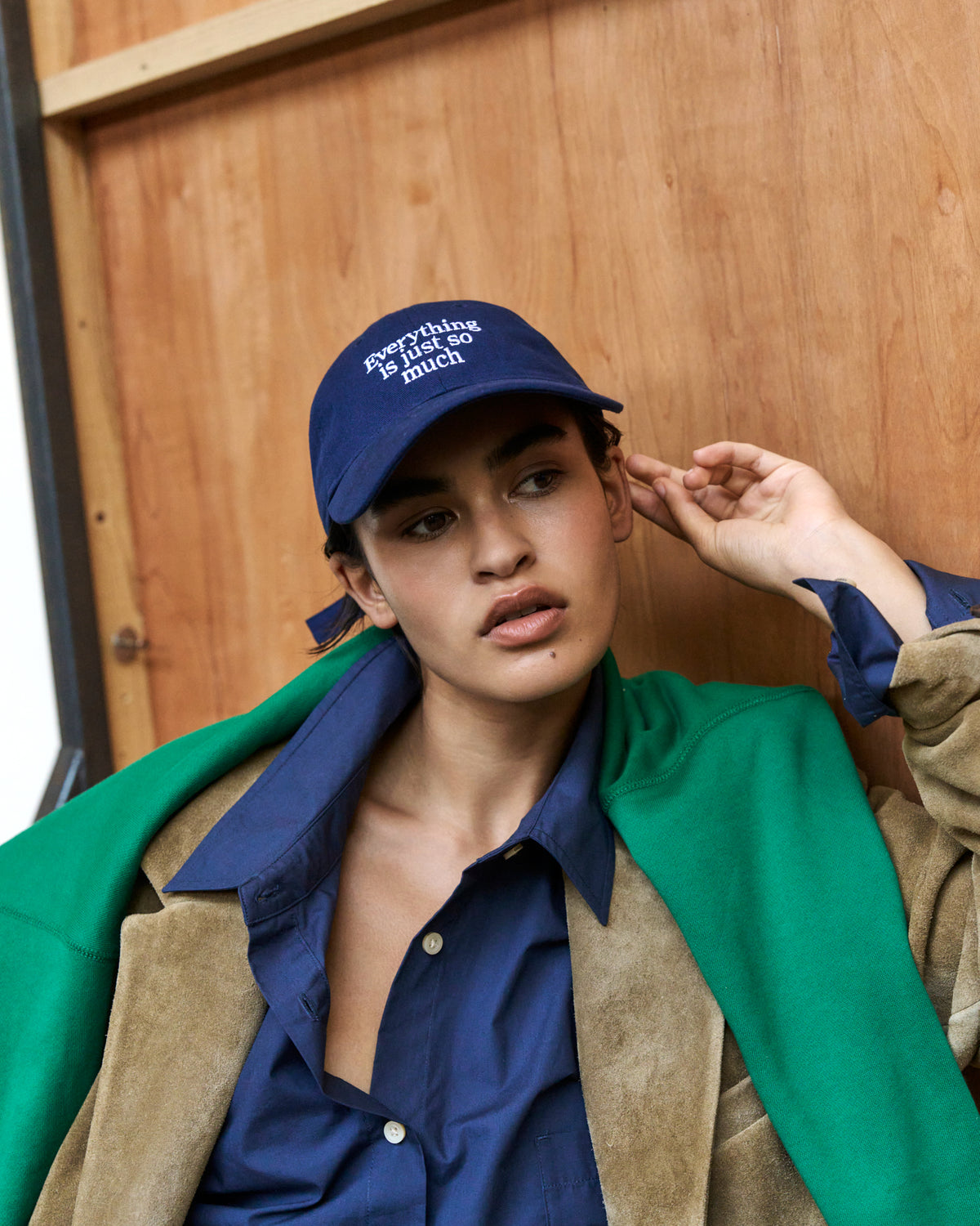 Woman adjusting the navy Artless Everything Is Just So Much organic cotton dad cap, denim shirt and green and tan jacket