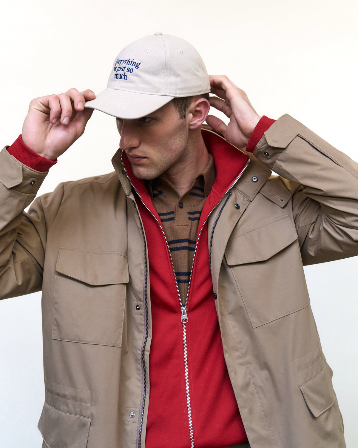 Man adjusting the sand Artless Everything Is Just So Much organic cotton dad cap, beige utility jacket over a red top