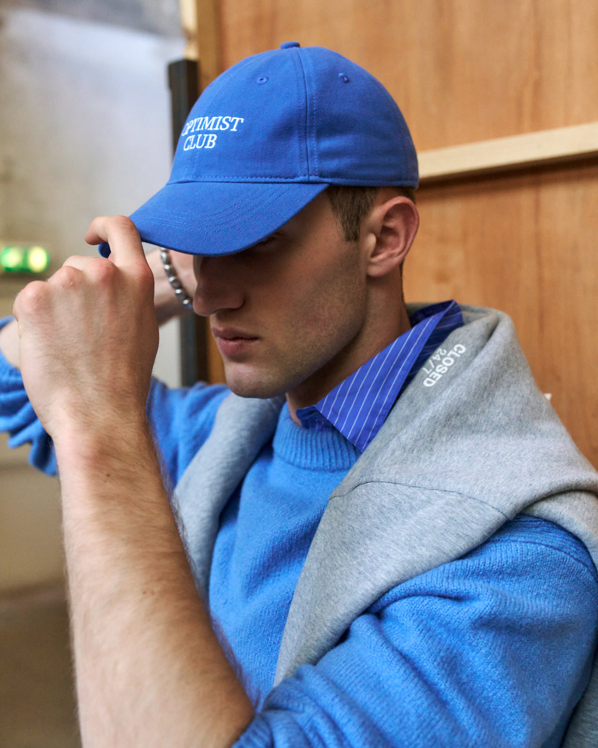 Man on the phone wearing the blue Artless Optimist Club organic cotton dad cap and a grey hoodie over a blue sweater