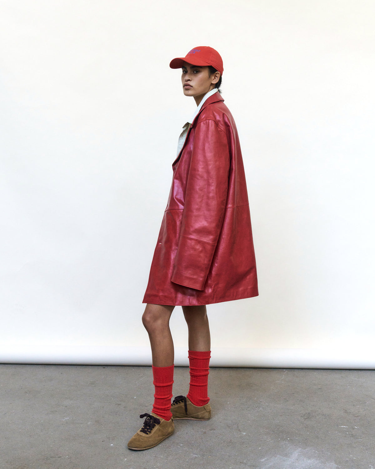 Person wearing the red Artless Optimist Club organic cotton dad cap with a red leather coat and red socks, full length
