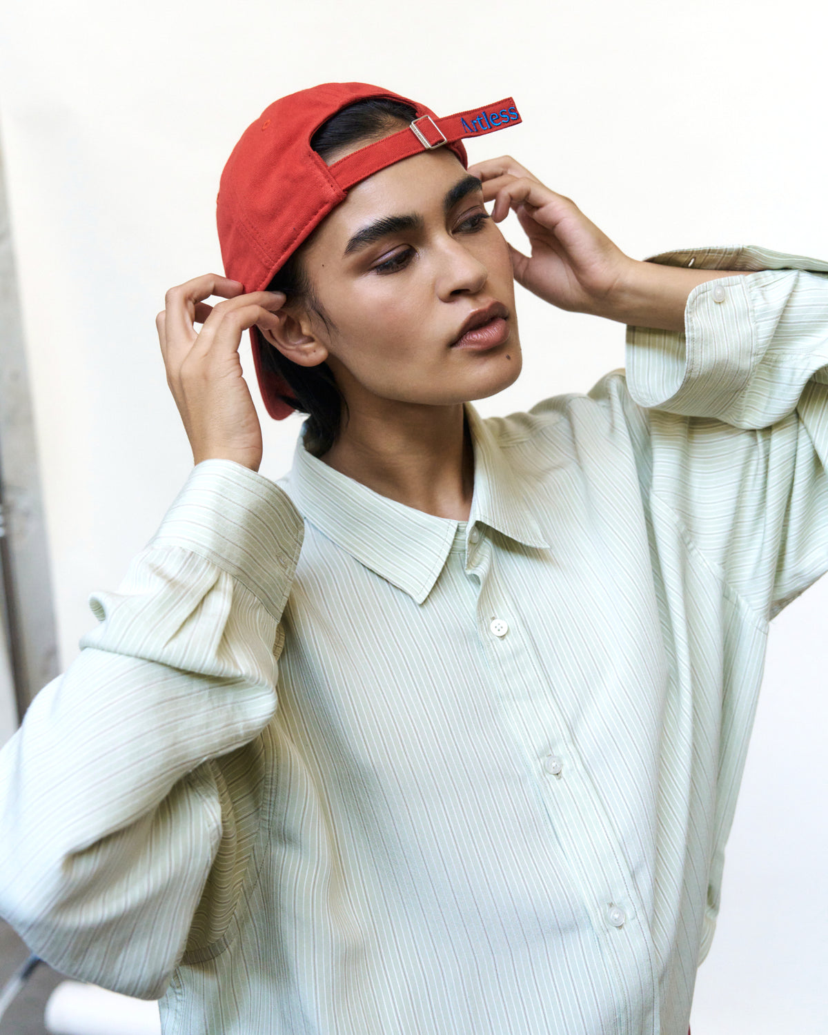 Person wearing the red Artless Optimist Club organic cotton dad cap backwards with a cream shirt