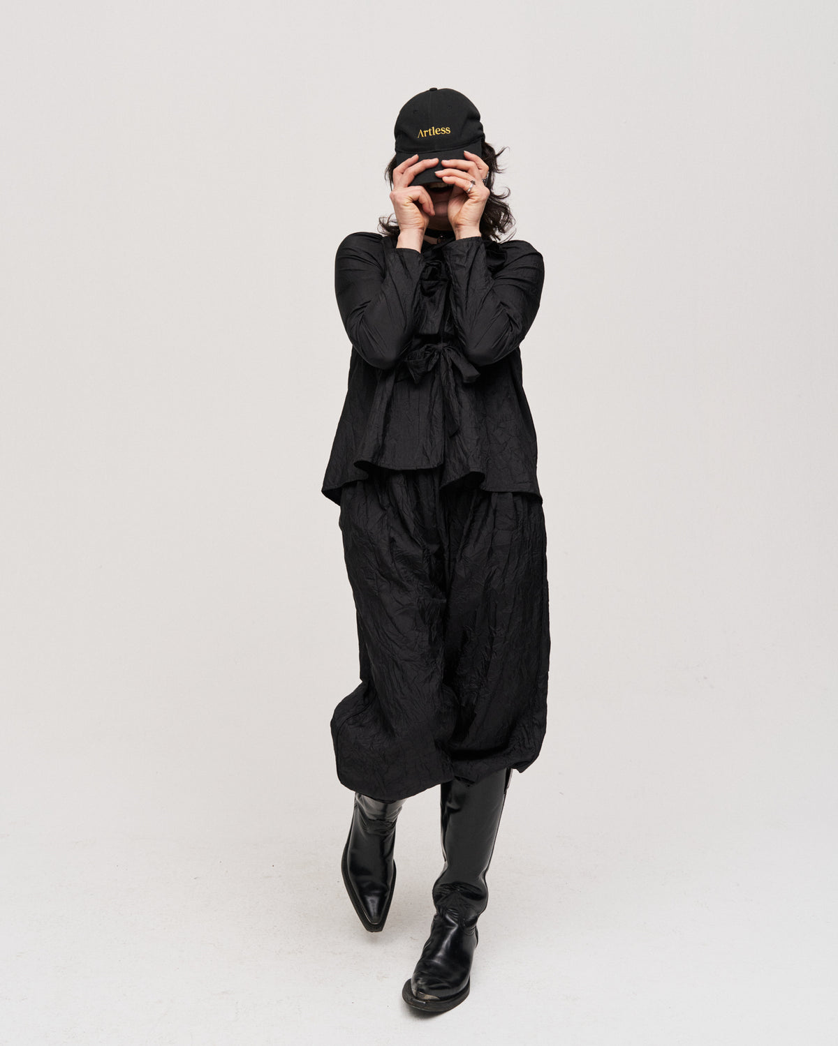 Person dressed in all black taking a photo while wearing the black Artless logo dad cap in GOTS certified organic cotton