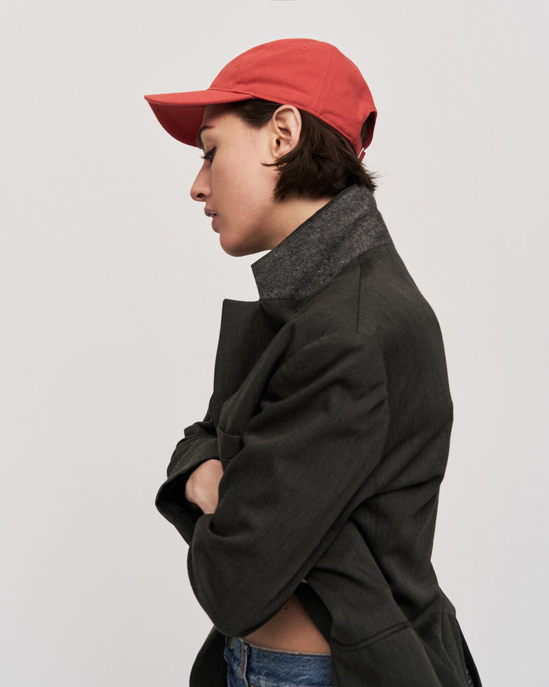 Person in profile with arms crossed wearing the red Artless organic cotton logo dad cap and a dark green coat