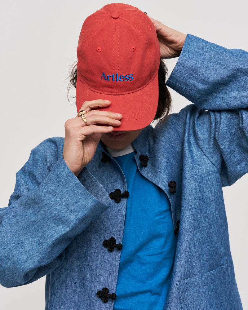 Person in a denim jacket holding the red Artless organic cotton logo dad cap up to their face