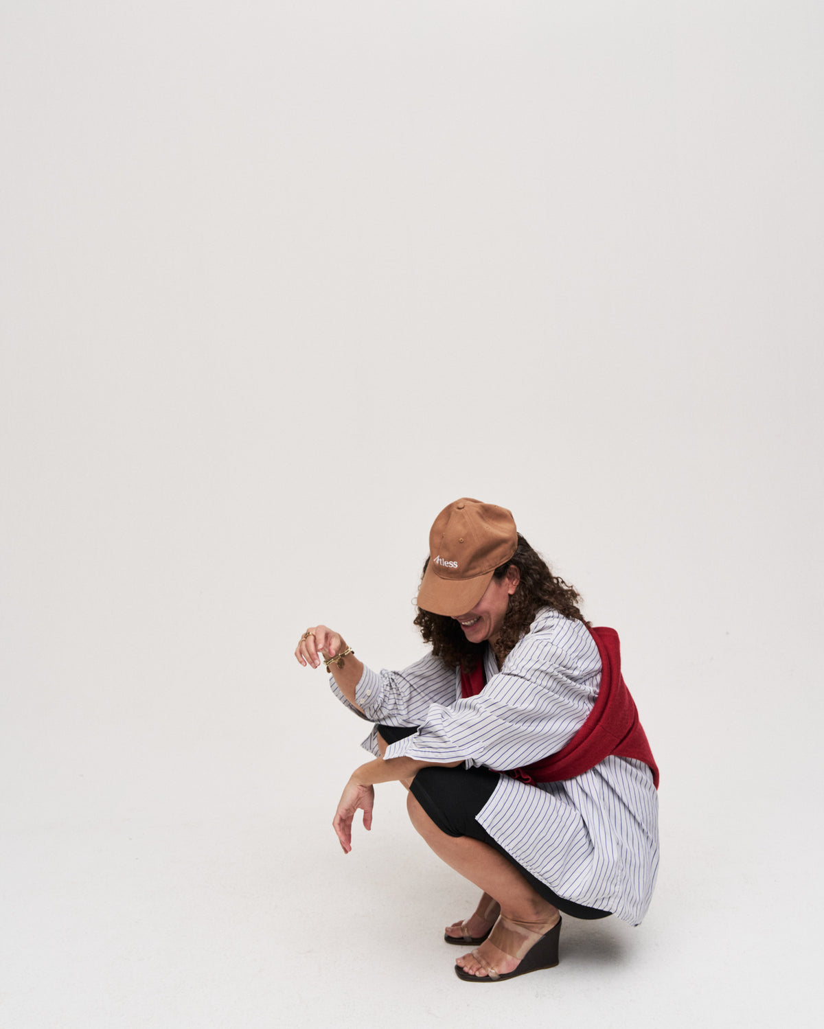 Person crouching while wearing the brown Artless organic cotton logo dad cap, white shirt and red waistcoat