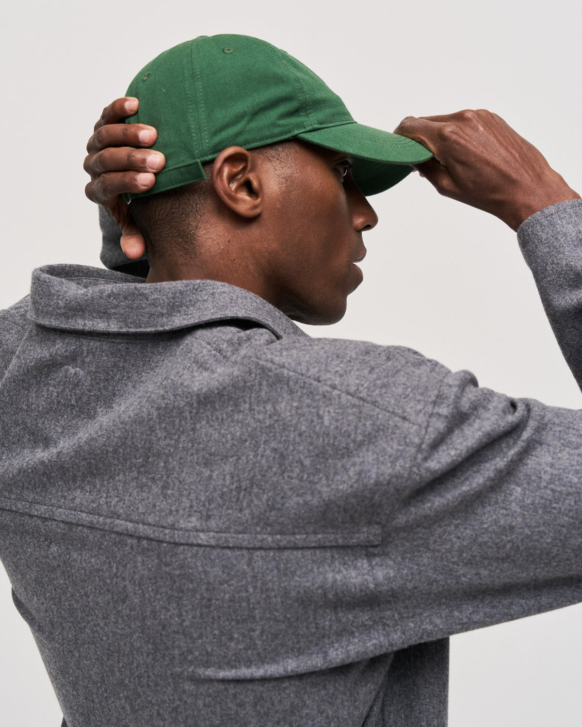 Man adjusting the green Artless organic cotton logo dad cap, grey wool coat, side view