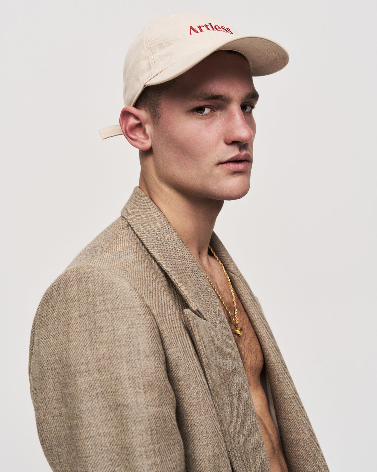 Young man in profile wearing the sand Artless organic cotton logo dad cap with a tweed blazer