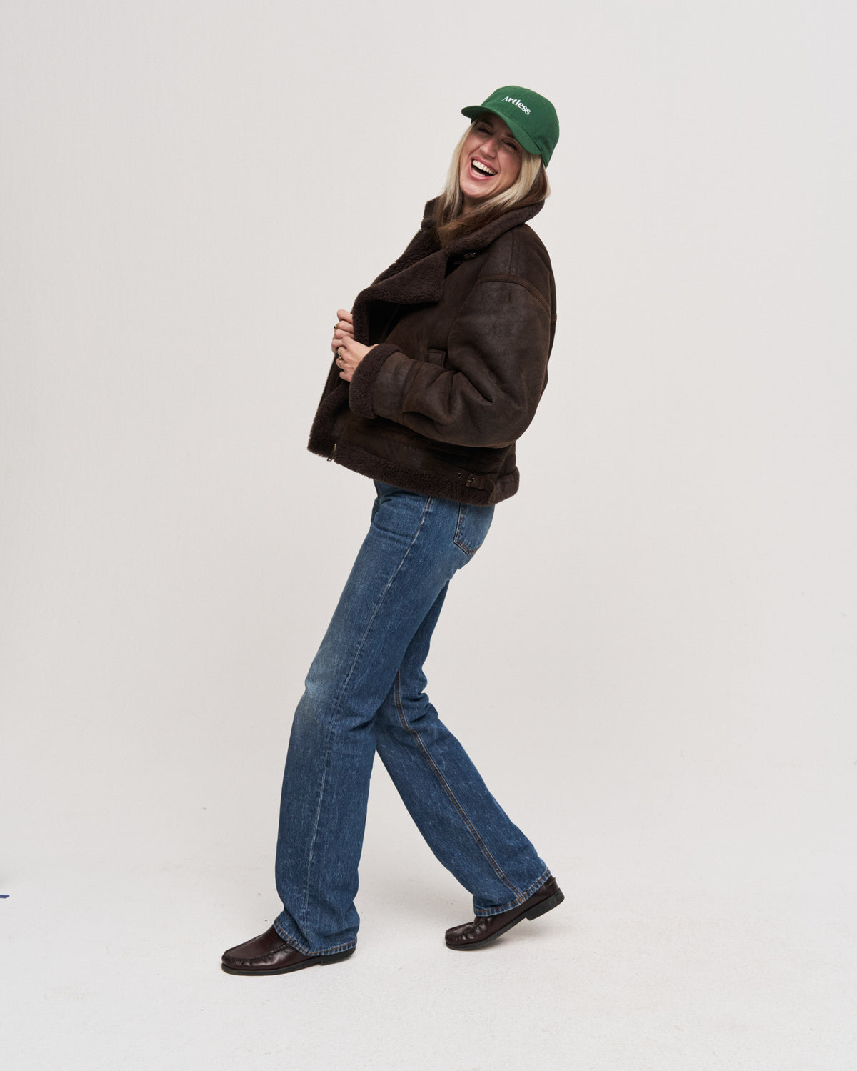 Woman walking and laughing while wearing the green Artless organic cotton logo dad cap with a brown leather jacket