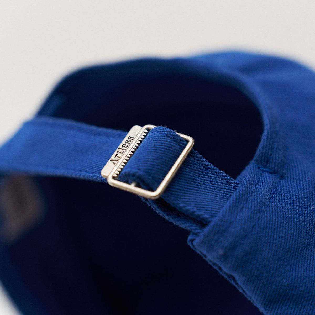 Close-up of the engraved Artless buckle on the blue unstructured 6-panel dad cap made from GOTS certified organic cotton