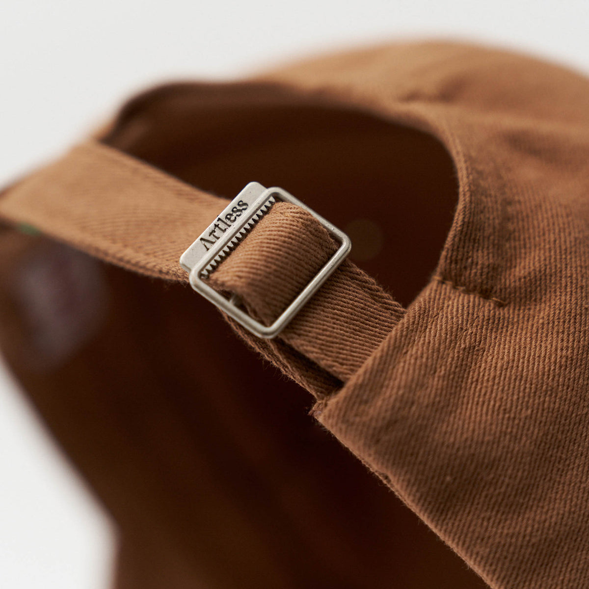 Close-up of the engraved Artless buckle on the brown unstructured 6-panel dad cap made from GOTS certified organic cotton