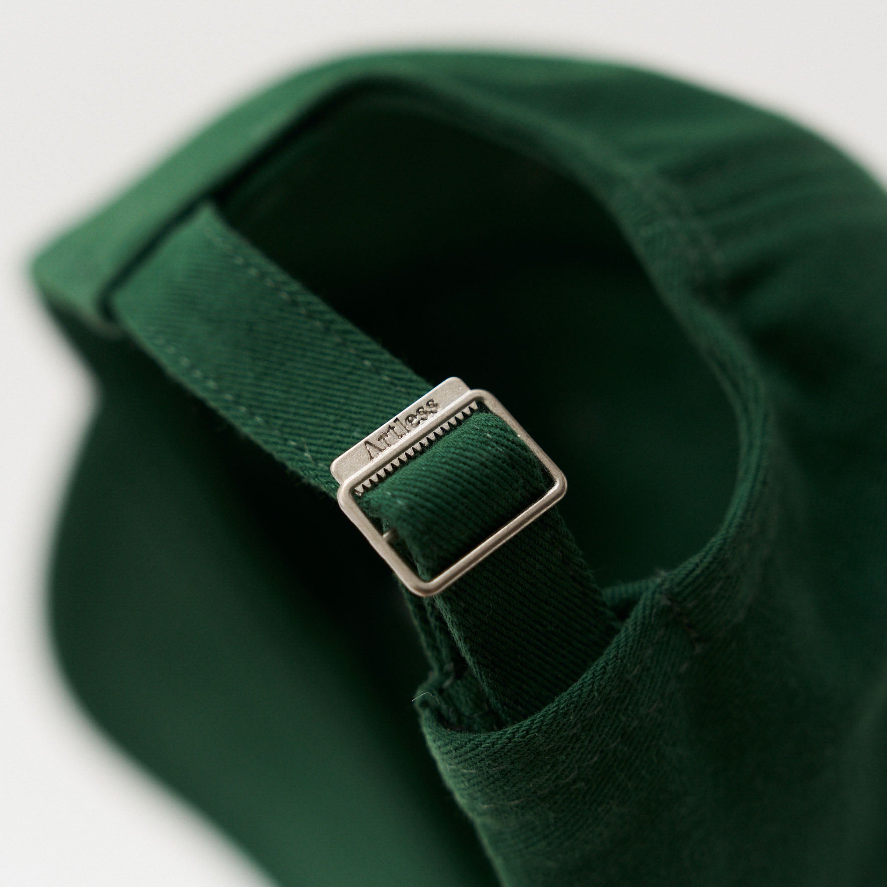 Close up of a artless engraved back buckle of the green unstructured 6-panel dad cap made from GOTS certified organic cotton by Artless
