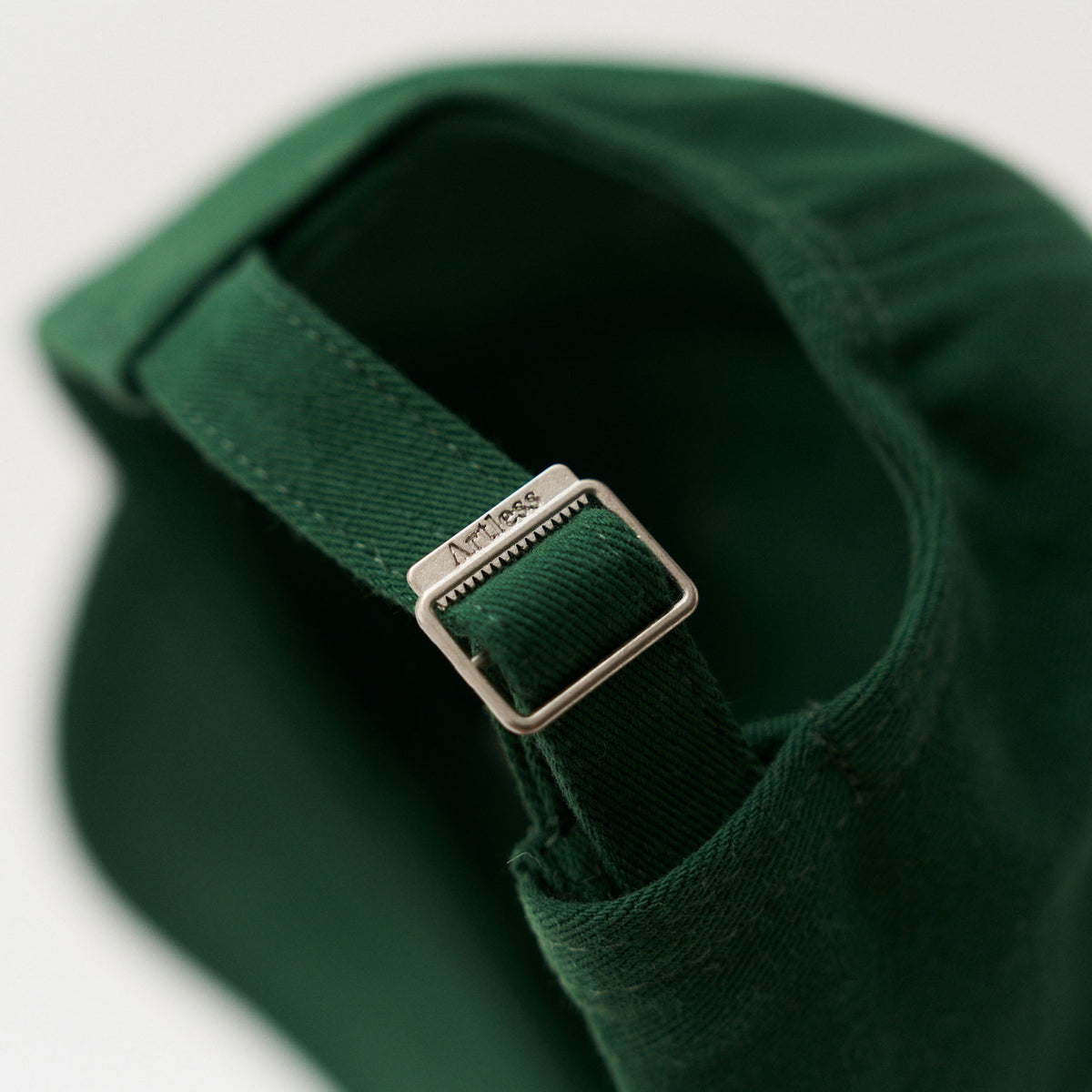 Close-up of the engraved Artless buckle on the green unstructured 6-panel dad cap made from GOTS certified organic cotton