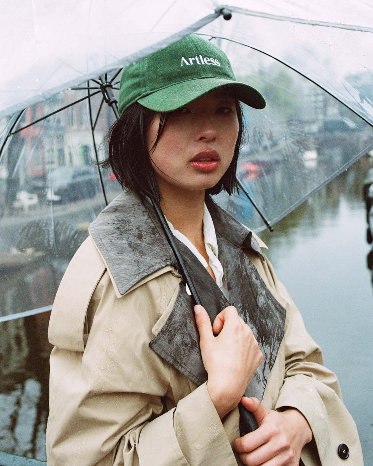 Person holding a transparent umbrella wearing a green unstructured 6-panel dad cap made from GOTS certified organic cotton by Artless