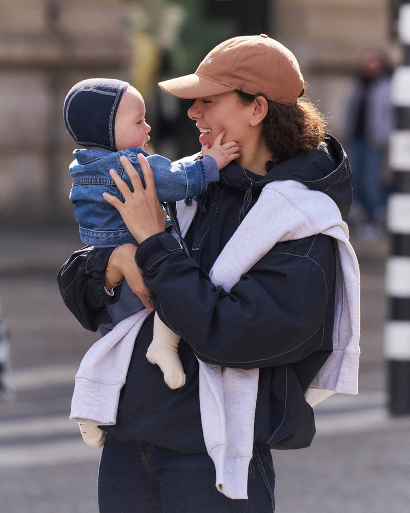 Woman holding a child on a street wearing a brown unstructured 6-panel dad cap made from GOTS certified organic cotton by Artless