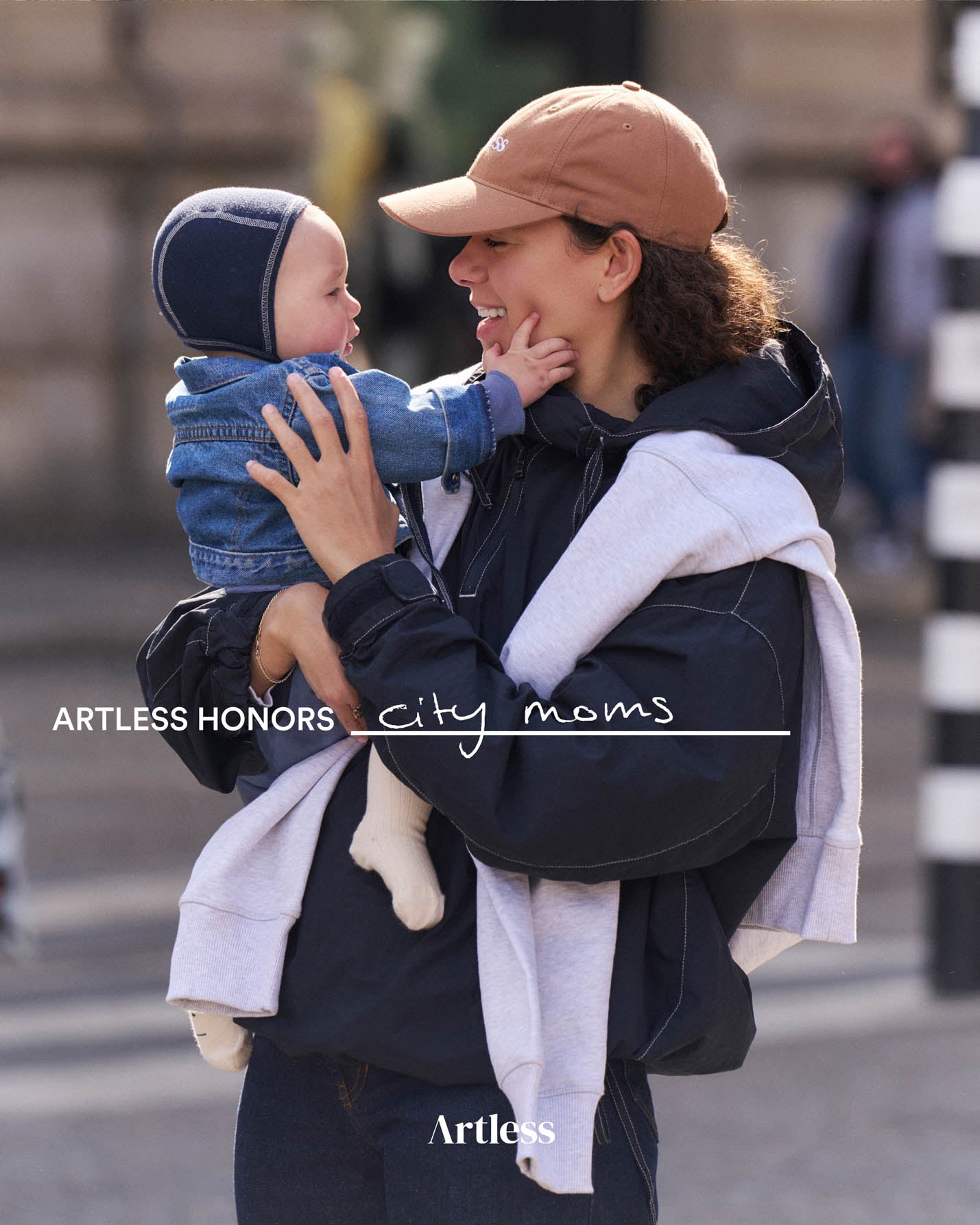 Woman holding a child on a city street wearing a brown unstructured 6-panel dad cap made from GOTS certified organic cotton by Artless