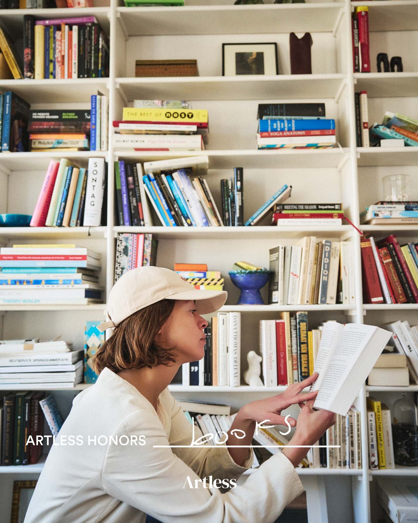 Person reading a book in a library with bookshelves filled with books wearing a sand coloured unstructured 6-panel dad cap made from GOTS certified organic cotton by Artless