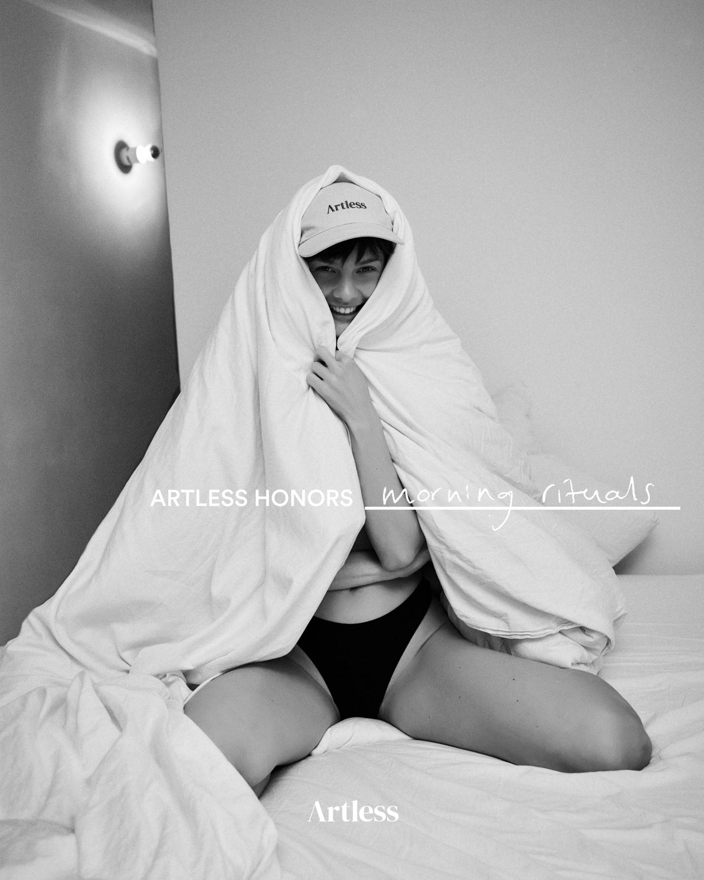 woman wrapped in a towel on a bed wearing a sand coloured unstructured 6-panel dad cap made from GOTS certified organic cotton by Artless