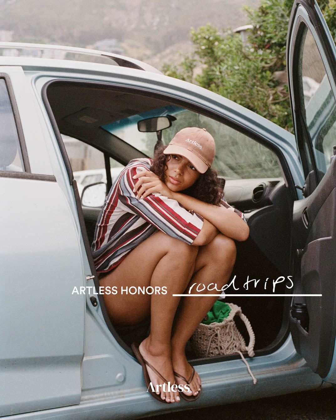 Woman sitting in an open car door wearing a brown unstructured 6-panel dad cap made from GOTS certified organic cotton by Artless