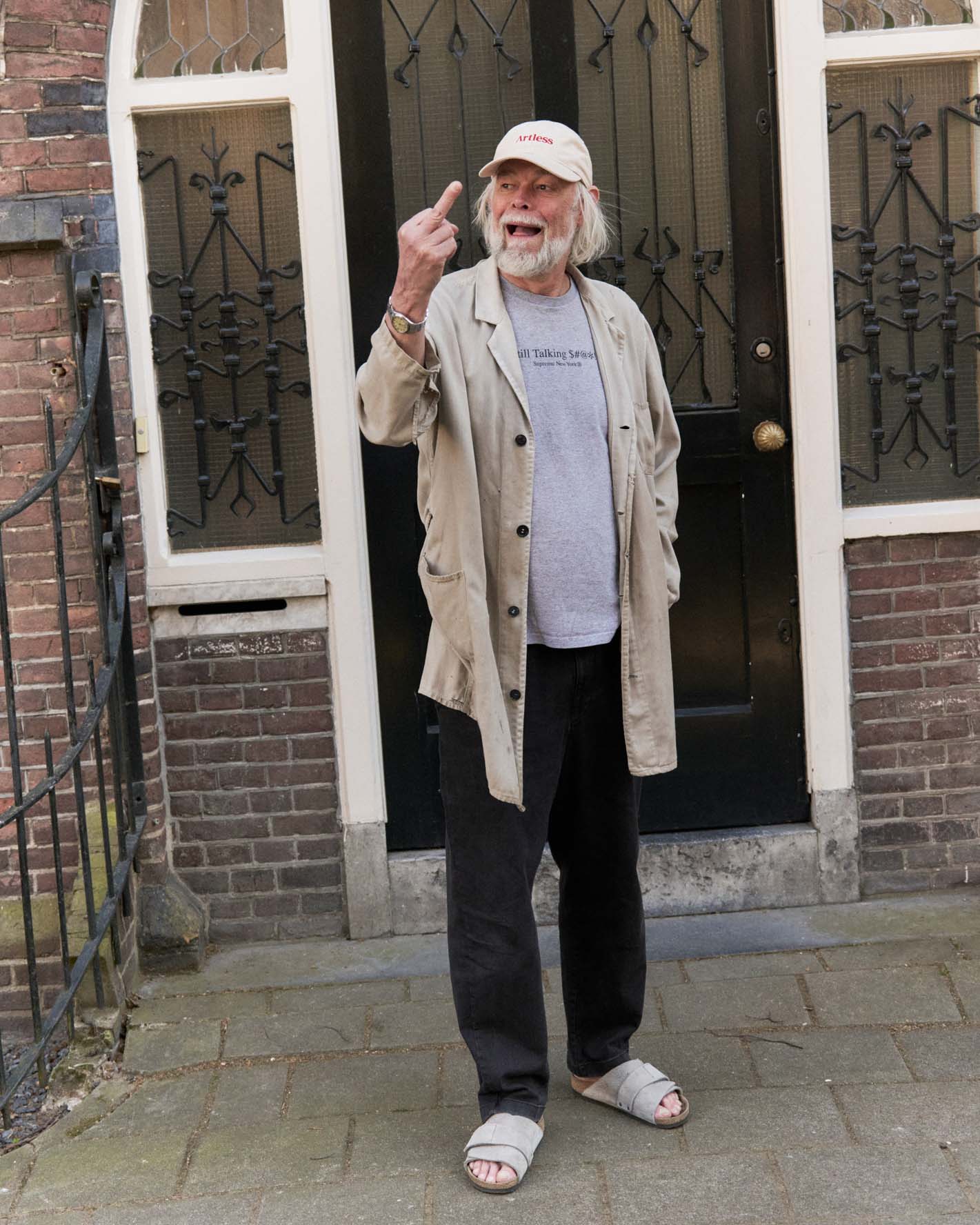 Man standing outside a building wearing a sand coloured artless GOTS organic dad cap giving the middle finger laughing