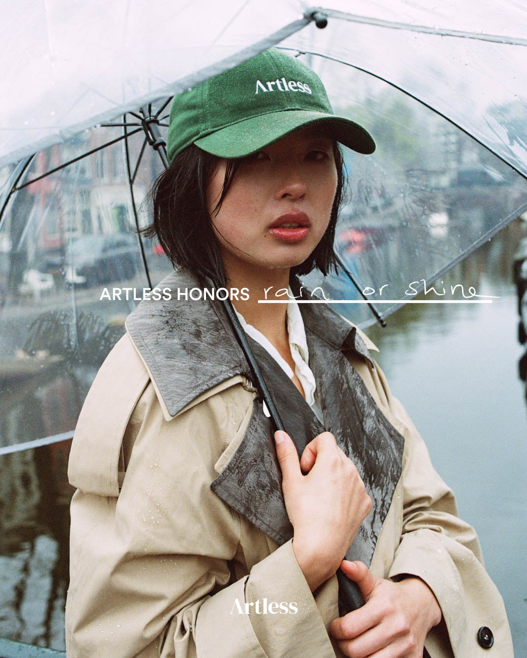 woman holding a transparent umbrella in the rain wearing a green unstructured 6-panel dad cap made from GOTS certified organic cotton by Artless