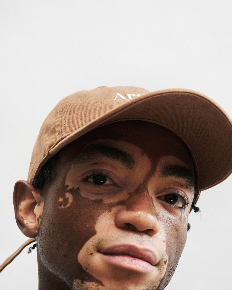 Person with vitiligo wearing a brown unstructured 6-panel dad cap made from GOTS certified organic cotton by Artless