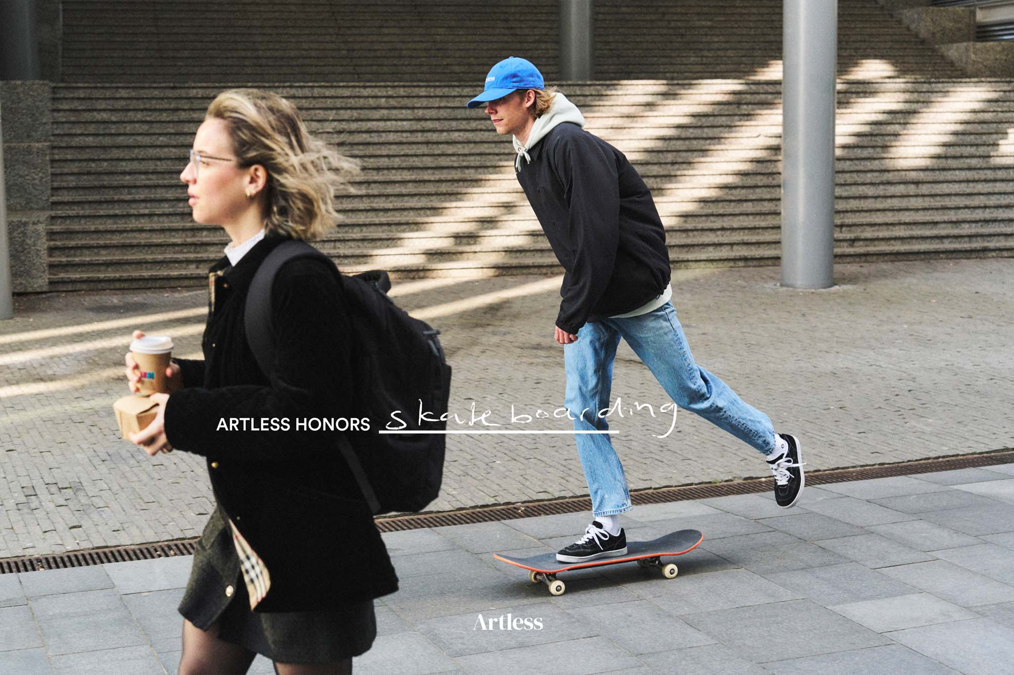 man skateboarding wearing a blue unstructured 6-panel dad cap made from GOTS certified organic cotton by Artless passing a woman on the street 
