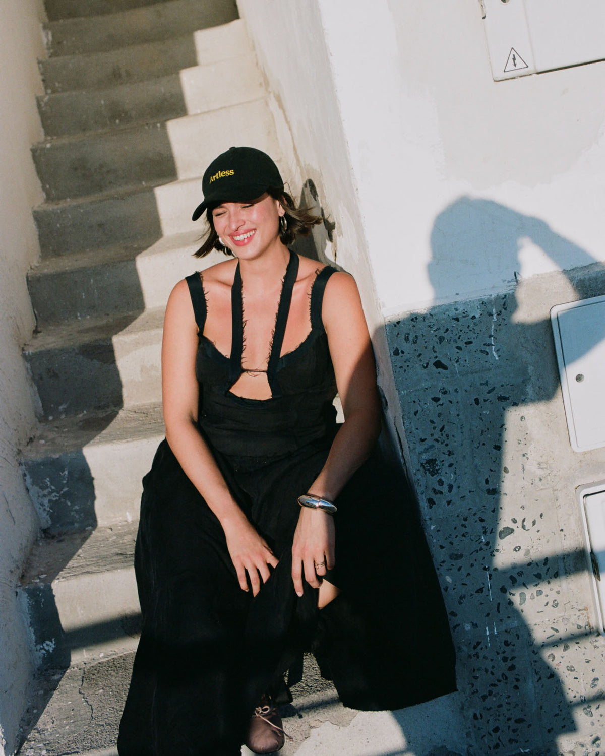 Woman laughing in the sun wearing a black unstructured 6-panel dad cap made from GOTS certified organic cotton by Artless