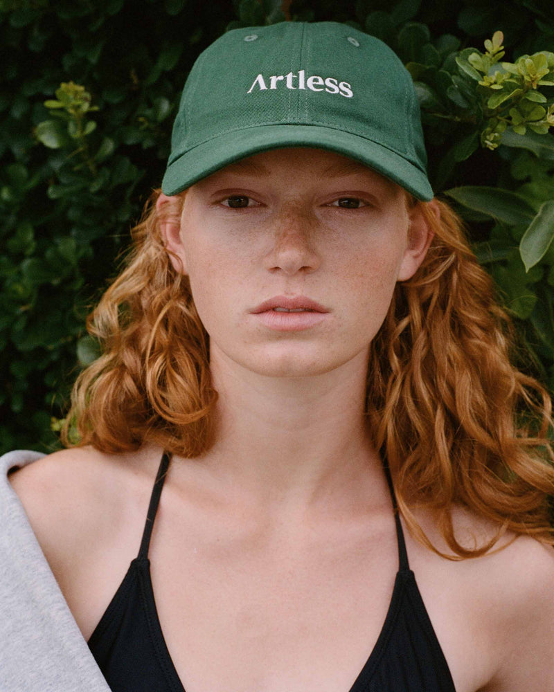Person wearing a green unstructured 6-panel dad cap made from GOTS certified organic cotton by Artless