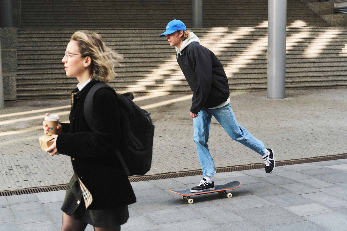 Skateboarder passing a woman on the street wearing a blue unstructured 6-panel dad cap made from GOTS certified organic cotton by Artless 