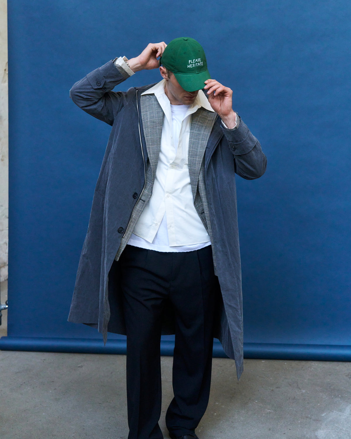 Man adjusting the green Artless Please Hesitate organic cotton dad cap, grey coat over a white shirt and dark trousers