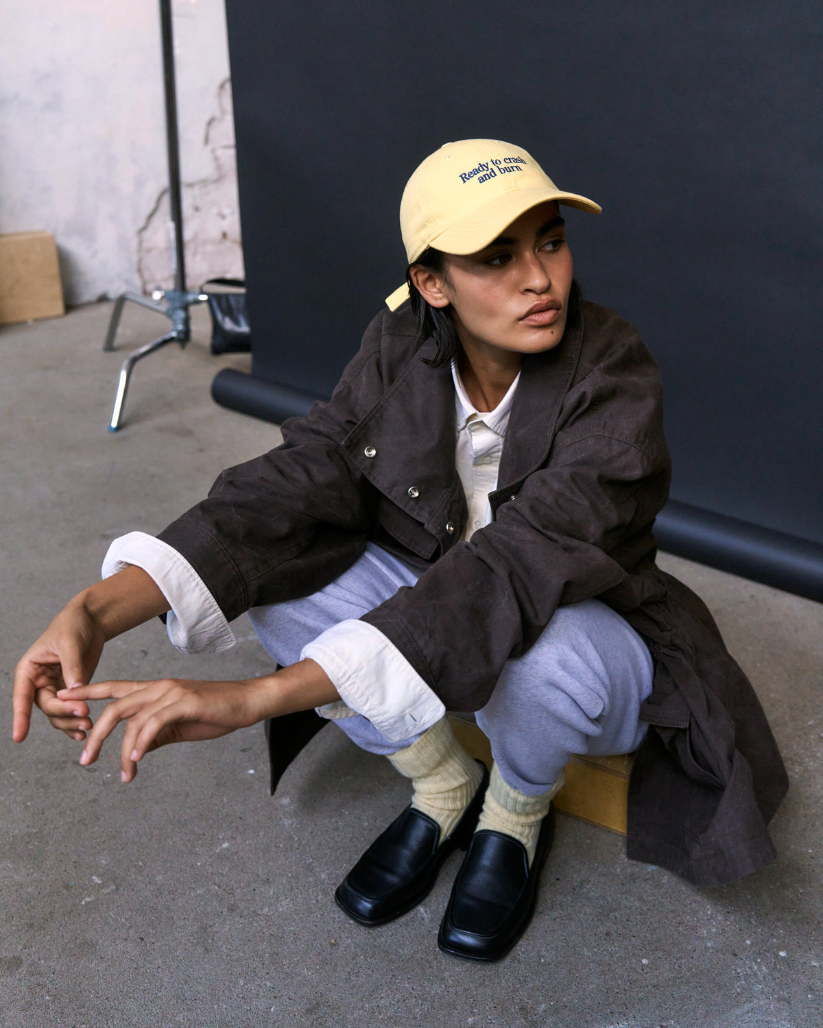 Person crouching while wearing the butter yellow Artless Ready To Crash And Burn organic cotton dad cap and a brown jacket