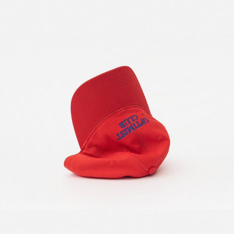 Red Artless Optimist Club organic dad cap, laying on its side