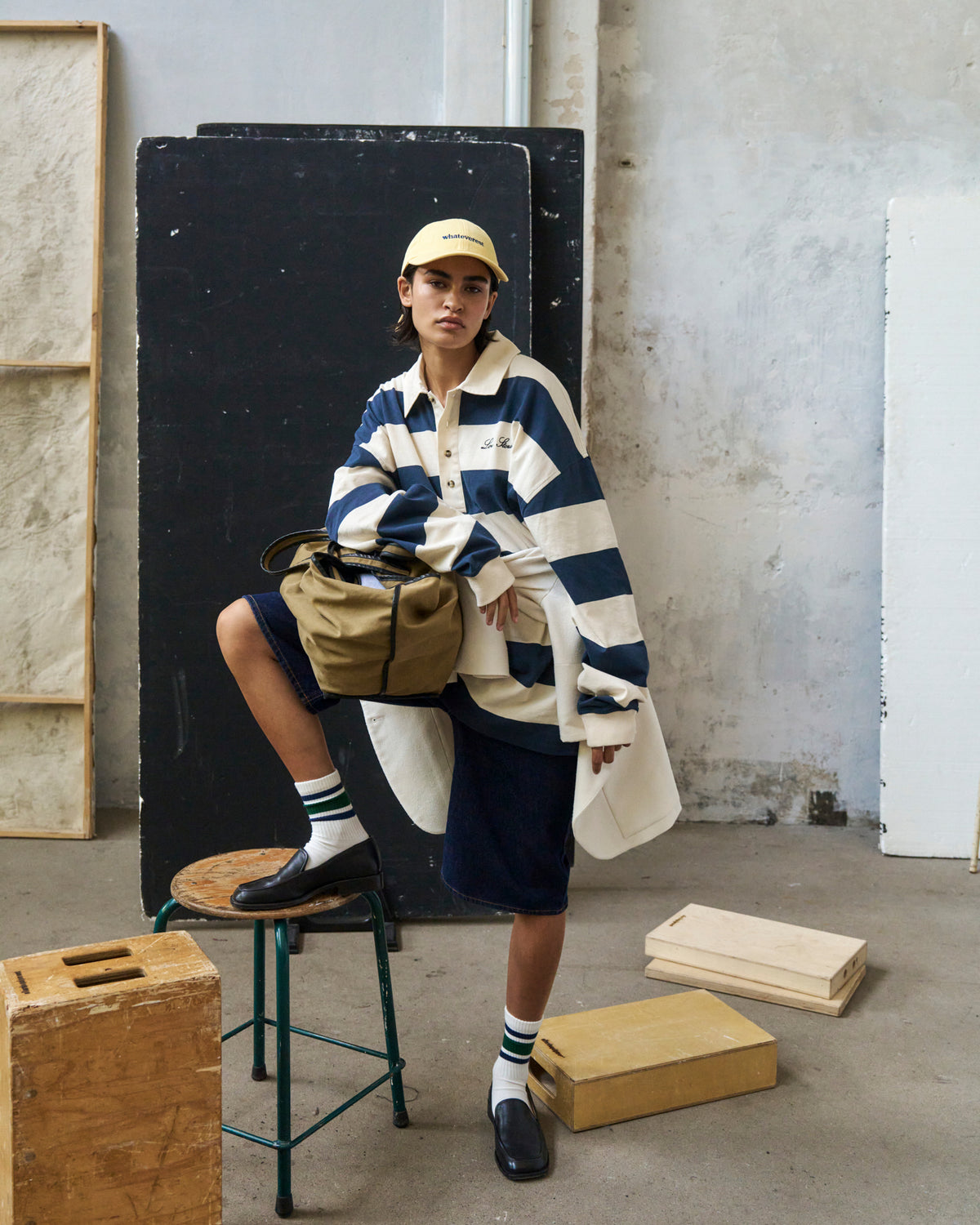 Person seated on a wooden block wearing the butter yellow Artless Whateverest organic cotton dad cap and a striped rugby shirt