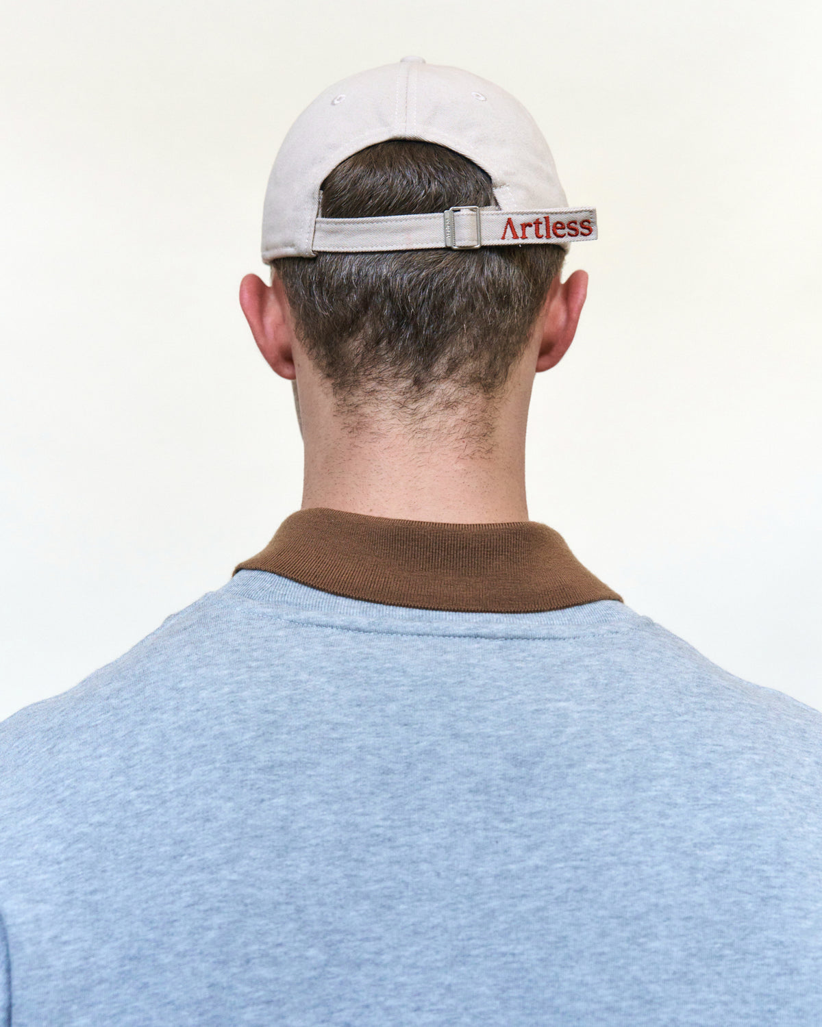 Back view of a man wearing the sand Artless You Barely Live Once organic cotton dad cap with the embroidered Artless strap and a grey sweater