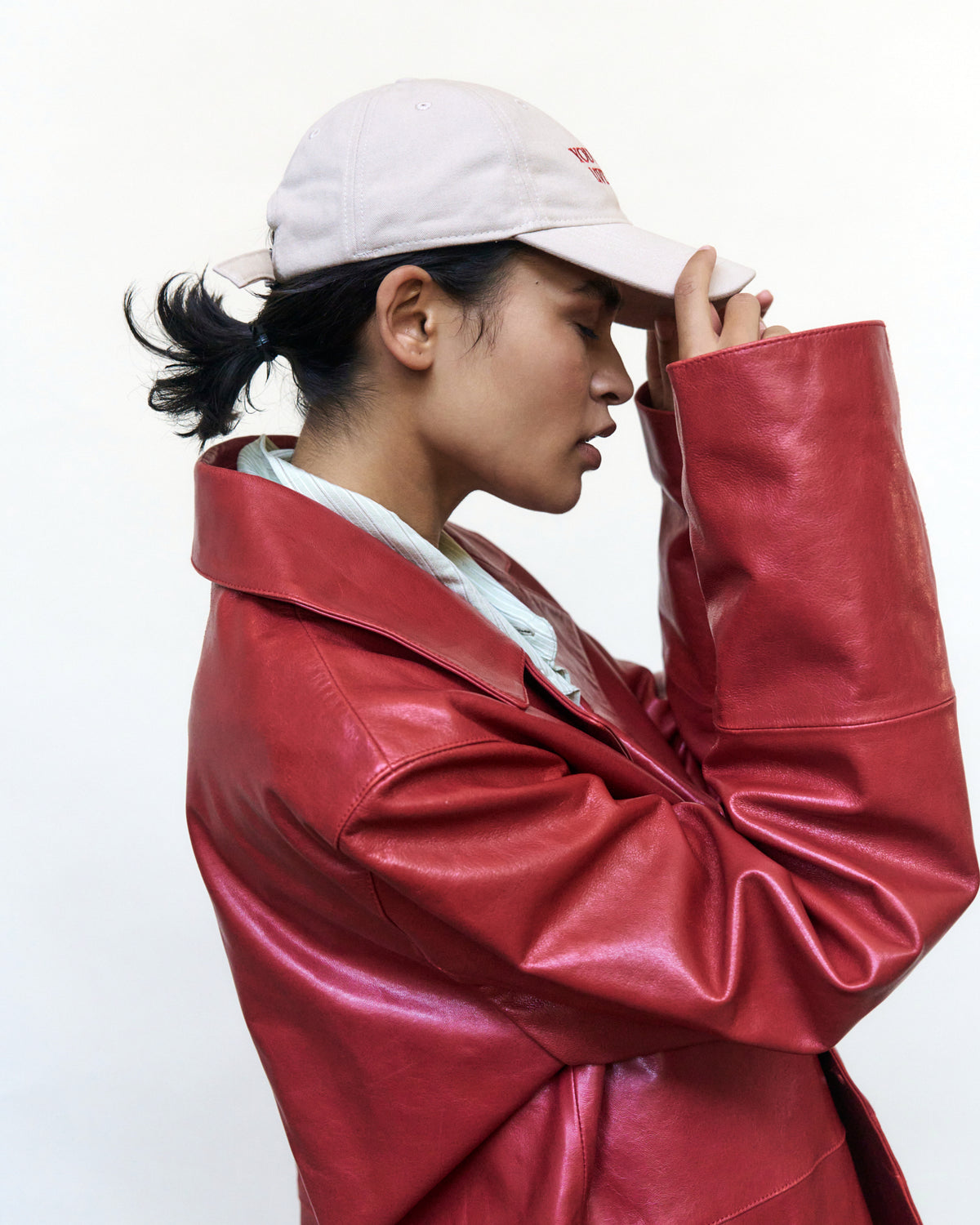 Woman in profile wearing the sand Artless You Barely Live Once organic cotton dad cap and a red leather jacket